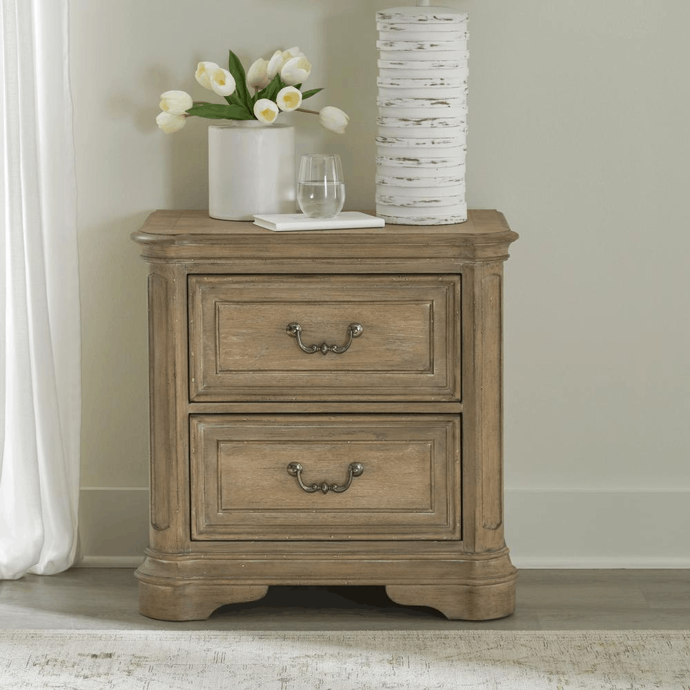 Magnolia Manor nightstand with Weathered Bisque finish and two drawers, adorned with white vase, flowers, and decorative pieces